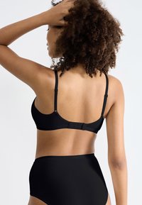 Ensemble de lingerie noire avec un design lisse et sans couture, des bretelles ajustables et une fermeture à crochets dans le dos. Texture du tissu douce.