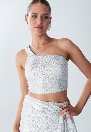 One-shoulder, cropped top in white adorned with sequins. Smooth texture, fitted design, paired with a matching skirt draped at the waist.