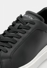 Schwarze Leder-Sneaker mit flachen schwarzen Schnürsenkeln, weißer Sohle und strukturierten Akzenten. Verfügt über dezente Markenkennzeichnung an der Zunge.