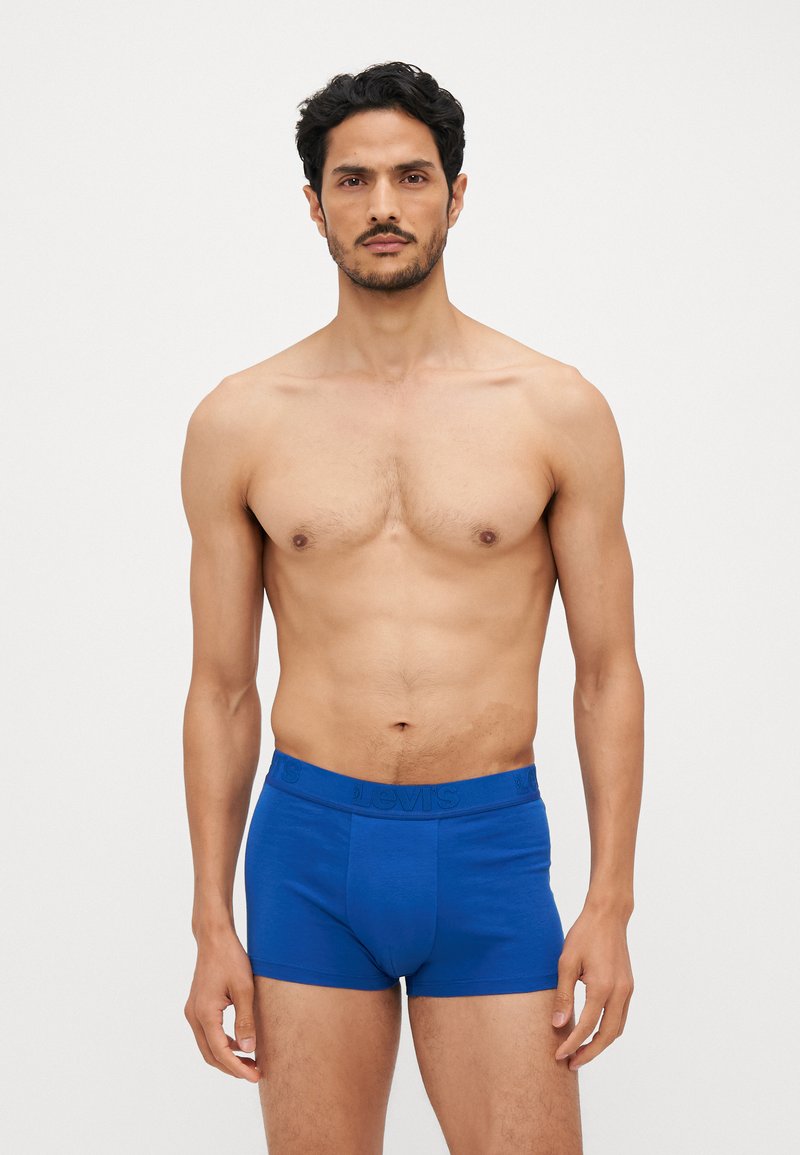 Boxers de algodão azuis com uma textura suave, apresentando um cós elástico com a marca e um ajuste justo, exibidos por um modelo num fundo neutro.