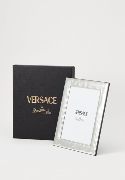 Rama foto Versace cu o margine argintie texturată, expusă lângă o cutie neagră cu inscripții aurii și detalii despre brand.