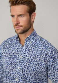Camisa azul con un diseño geométrico y acentos blancos, con cuello abotonado y tejido texturizado.
