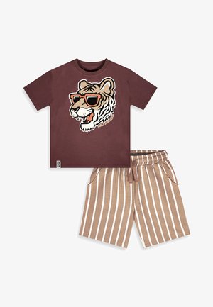 T-shirt marrone a maniche corte con grafica di una tigre che indossa occhiali da sole e la scritta "Wild and Cool", abbinata a pantaloncini beige e bianchi a righe verticali.