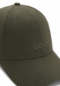 Olive green baseball cap made of textured fabric, featuring an embroidered "BOSS" logo on the front and a rounded crown.