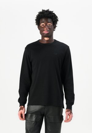 Black long-sleeve shirt made of cotton, featuring a crew neckline and subtle logo, paired with shiny black cargo pants.