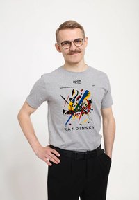 Šedé bavln�ěné tričko s grafikou inspirovanou Kandinským v červené, modré, zelené a žluté barvě; kulatý výstřih a krátké rukávy, doplněné černými kalhotami.