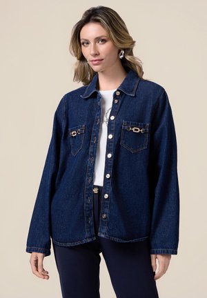 Giacca camicia in denim blu scuro, con due tasche frontali con hardware dorato, chiusura con bottoni e una vestibilità comoda. Texture liscia.