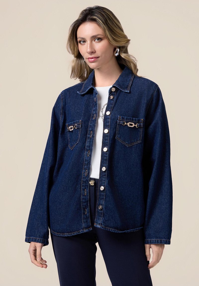 Jachetă din denim de culoare bleu închis, cu două buzunare frontale și accesorii aurii, închidere cu nasturi și croială lejeră. Textură netedă.