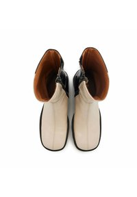 Bottines en cuir noir et blanc avec une finition lisse, textures contrastantes et doublure intérieure marron. Équipées de fermetures éclair sur le côté et de semelles plates.