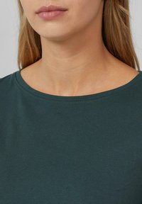 Dark green t-shirt featuring a wide, rounded neckline and a smooth, soft texture. Visible stitches along the neckline enhance its design.
