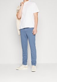 Jasnoniebieskie spodnie wykonane z miękkiego materiału, o dopasowanym kroju, z gładką fakturą. Połączone z białym t-shirtem i beżowymi trampkami.