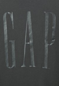 T-shirt in cotone nero con grandi lettere metalliche lucide che spellano "GAP" nella parte anteriore, con una finitura in tessuto testurizzato.