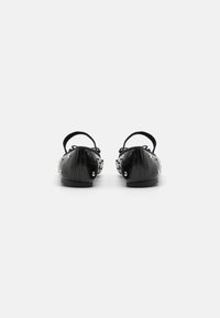 Bailarinas negras de cuero con acentos de tachuelas y un detalle de lazo. Presentan un tacón bajo y un diseño de punta redondeada. Vista trasera mostrada.