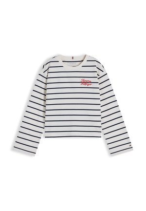 Chemise blanche à manches longues avec des rayures horizontales noires, texte rouge "Tommy Hilfiger" sur la poitrine, et petit logo sur le poignet de la manche gauche.