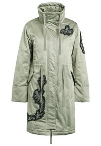 Cappotto trapuntato verde con colletto alto, tasche laterali e motivo a foglia ricamato in nero sulla parte anteriore. Presenta lacci per la regolazione.