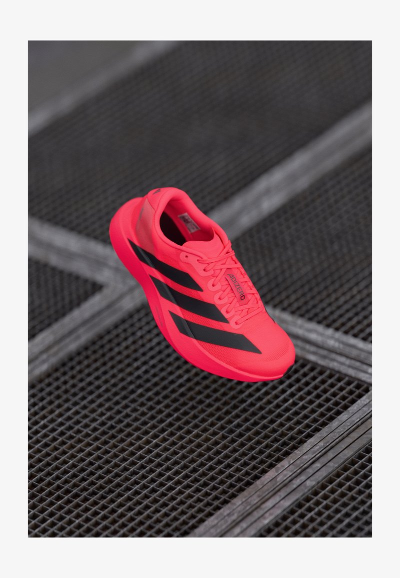 Bright pink running shoe with black stripes, made of lightweight mesh material, featuring a textured sole and lace-up design.