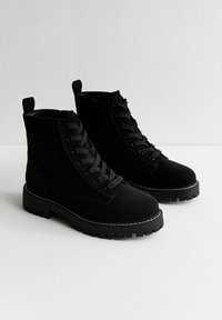 Bottines en suède noir avec un design à lacets, dotées d'une doublure en fausse fourrure, d'un embout rond, d'une semelle robuste et de coutures blanches contrastantes.