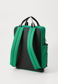 Zaino verde e nero con spallacci imbottiti, un compartimento principale con zip, tasca laterale e accenti del manico in bianco e nero a contrasto.