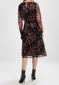 Černé květované šaty s průhlednými dlouhými rukávy, zeštíhleným pasem a sukní do poloviny lýtek. Obsahují barevné vzory listů a detail s otevřenými zády.