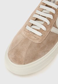 Lys brun semsket sneaker med hvite lisser, rund tå og teksturert gummisåle. Har sømde detaljer og en subtil logo på siden.