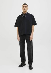 Camiseta de algodón negra con un corte relajado y mangas cortas, combinada con unos vaqueros de mezclilla negros. Los accesorios incluyen una bufanda oscura atada alrededor del cuello.