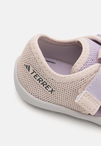 Zapatilla de malla rosa claro con parte superior texturizada, suela de goma, acentos en lavanda contrastantes y un logo "Terrex" en el lateral.