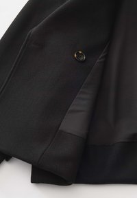 Blazer nero con tessuto esterno testurizzato, dotato di foderatura interna liscia. Include un bottone nero arrotondato e rever strutturati.