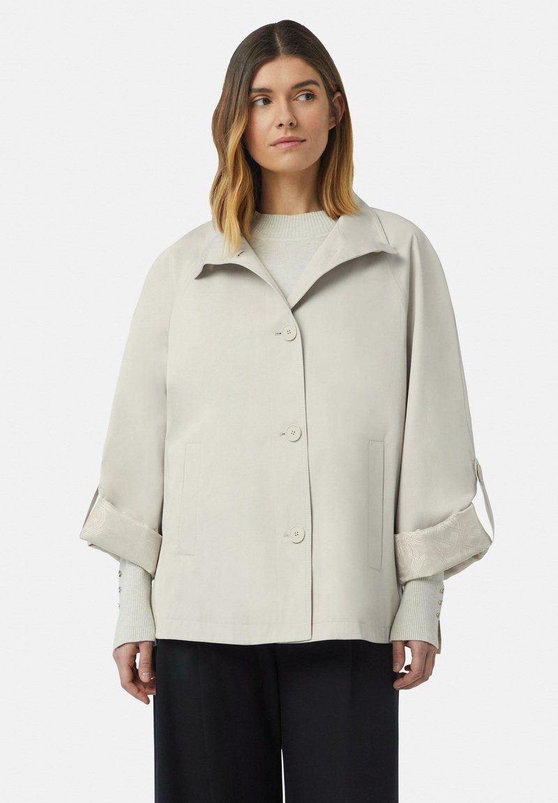 Veste structurée gris clair avec col, fermeture à bouton, poches latérales et poignets à motif retroussés. Texture lisse avec une coupe ajustée.