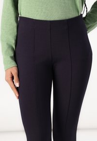 Høye midje, marineblå leggings laget av et glatt, elastisk stoff. Har detaljer med sømmer foran og en tettsittende silhuett.
