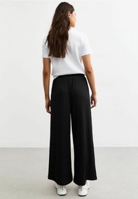 Zwarte geplooide broek met een hoge tailleband, losse pasvorm en zachte textuur, gecombineerd met een wit T-shirt en witte sneakers.