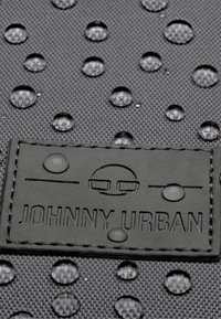 Fekete textúrájú anyag vízcseppekkel. Bőr restitúció, amelyen a "JOHNNY URBAN" logó van dombornyomva az alsó jobb sarokban. Vízálló kialakítás.