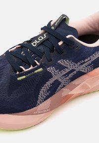 Chaussure de course avec un dessus en tricot bleu marine, un col ressemblant à une chaussette rose et une semelle intermédiaire texturée. Comprend des accents verts et un détail de logo visible.