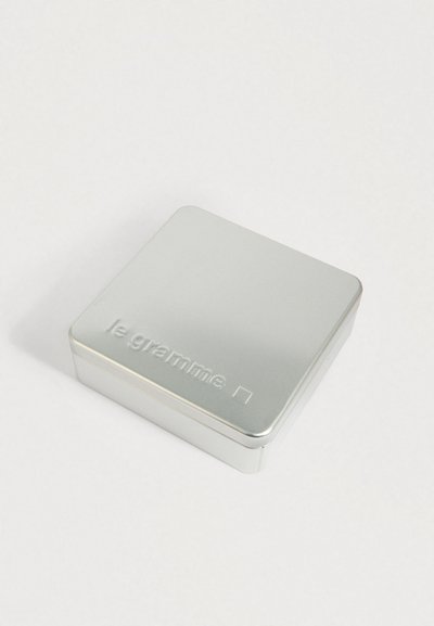 Kis ezüst fém doboz lekerekített szélekkel, a tetején a "le gramme" felirattal, sima fehér háttéren elhelyezve.