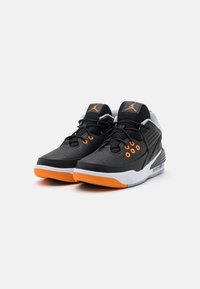 Zapatillas deportivas negras con acentos naranjas, que presentan una parte superior perforada, suela acolchada y el logo distintivo en la lengüeta. Suela intermedia blanca en contraste.