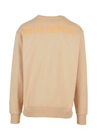 Beige hettegenser med lange ermer, ribbestrikkede mansjetter og rund halsåpning. Har kraftig oransje tekst "9N1M SENSE" på baksiden.
