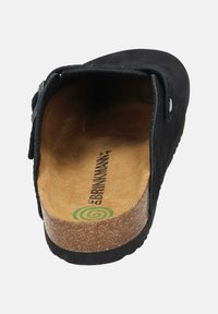 Black slip-on clog with cork sole, adjustable strap with buckle, and padded tan insole marked with brand name and green spiral logo.