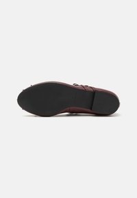 Chaussure en cuir bordeaux avec une surface lisse, dotée d'un nez arrondi et d'une semelle en caoutchouc noir. Des détails de boucle ajoutent une touche subtile.