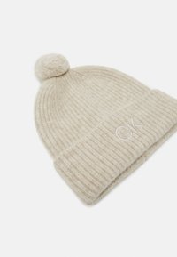 Berretto lavorato a maglia beige con texture a costine, dotato di un pompon sulla parte superiore e 'CK' ricamato in colore chiaro sul bordo piegato.