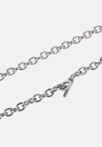 Ezüst színű fém lánc, kerek szemekből áll, kapcsolódobozzsal a záráshoz. A felülete sima és fényes, egységes fémes kivitelű.