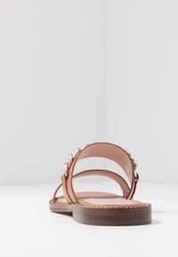 Bruine leren sandaal met een platte zool, voorzien van een ontwerp met twee brede banden en een kettingdetail aan de buitenkant. Glad, minimalistisch textuur.