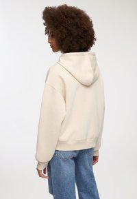 Kremowa bluza z kapturem z opuszczonymi ramionami i ściągaczem na dole, zestawiona z dżinsami o wysokim stanie z luźnym krojem.