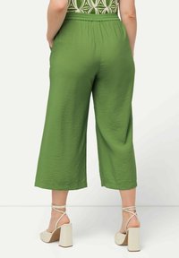 Groene, wijde broek met een gestructureerde stof en een elastische tailleband, gecombineerd met lichtgekleurde sandalen op een blokhak.
