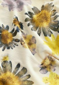 Le tissu floral présente de grandes fleurs bleues, jaunes et brunes sur un fond doux de couleur crème avec une finition texturée.