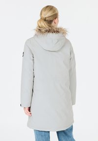 Hellgrauer langer Parka mit Kapuze, ausgestattet mit einem Pelzbesatz, seitlichen Taschen und einem abgerundeten Saum. Glatte Stofftextur.