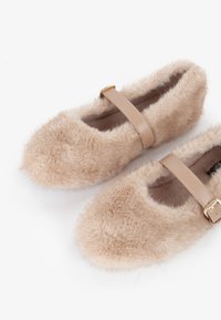 Scarpe beige soffici con punta arrotondata, dotate di una cinghia color marrone e una fibbia dorata. Tessuto morbido con un aspetto accogliente.