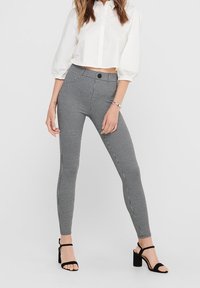 Zwart-witte houndstooth legging, hoog in de taille met een gladde textuur, gecombineerd met een kort wit shirt en zwarte open hakken.