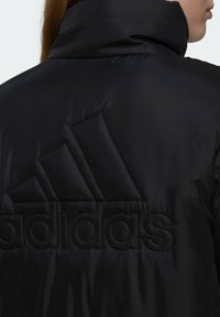 Doudoune noire avec un col montant, une texture mate et un logo Adidas brodé proéminent à l'arrière avec un design géométrique.