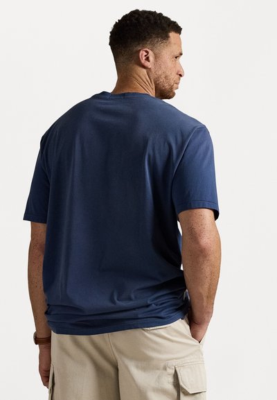 Tricou din bumbac bleu închis, cu mâneci scurte, croială lejera și guler rotund, purtat cu pantaloni scurți cargo bej. Design minimalist, textură netedă.