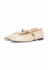 Ballerine in vernice beige con punta rotonda, una fascia decorativa sul collo del piede e un piccolo dettaglio a fibbia. Suola piatta con grip minimale.