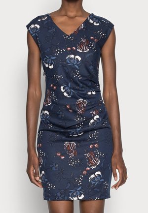 Femme portant une robe bleu marine sans manches avec un imprimé floral dans des tons blancs, marron et bleus.